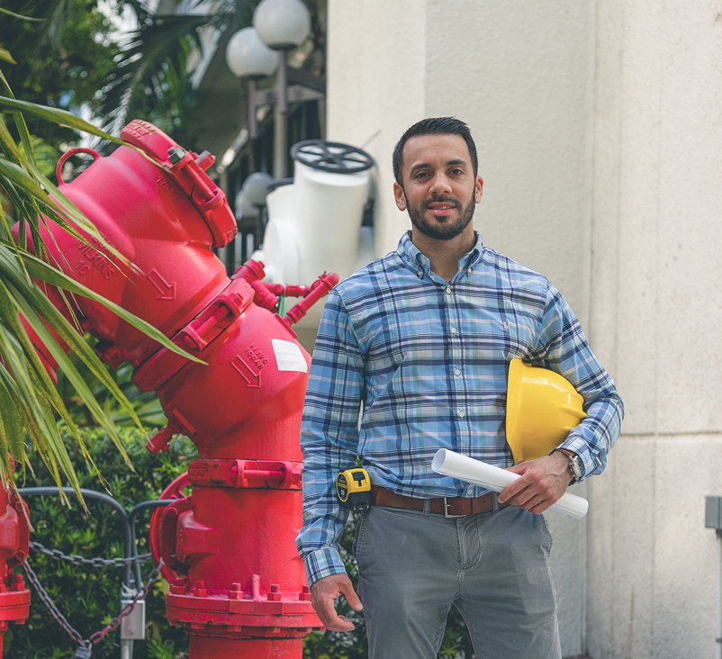 Alejandro is standing next to a big red pipe.