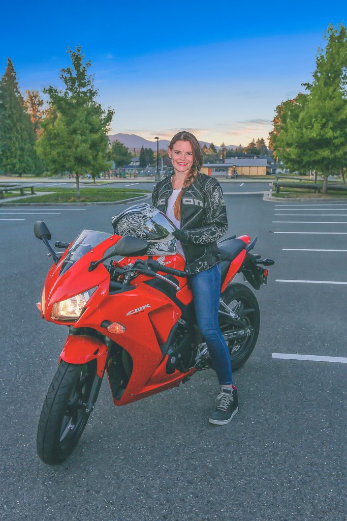 Jess is smiling at the camera while on top of her red motorbike.