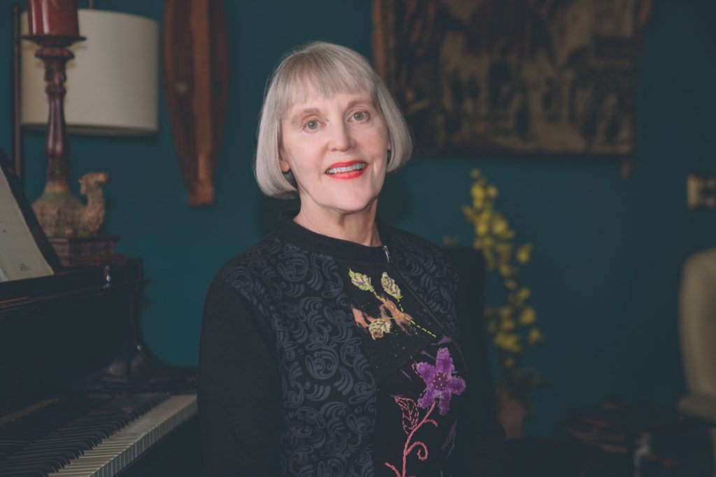 Renee is sitting by the piano. You can see joy in her eyes. She smiles.