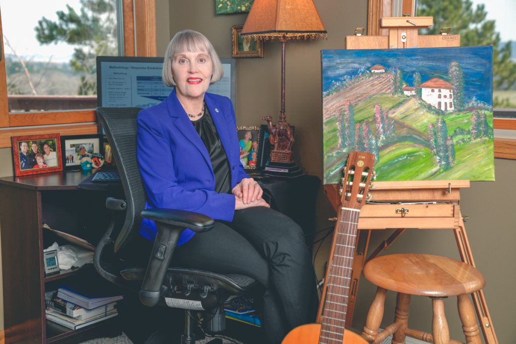 Renee is sitting next to a beautiful painting. Below the painting is a musical instrument. It looks like a classical guitar. 