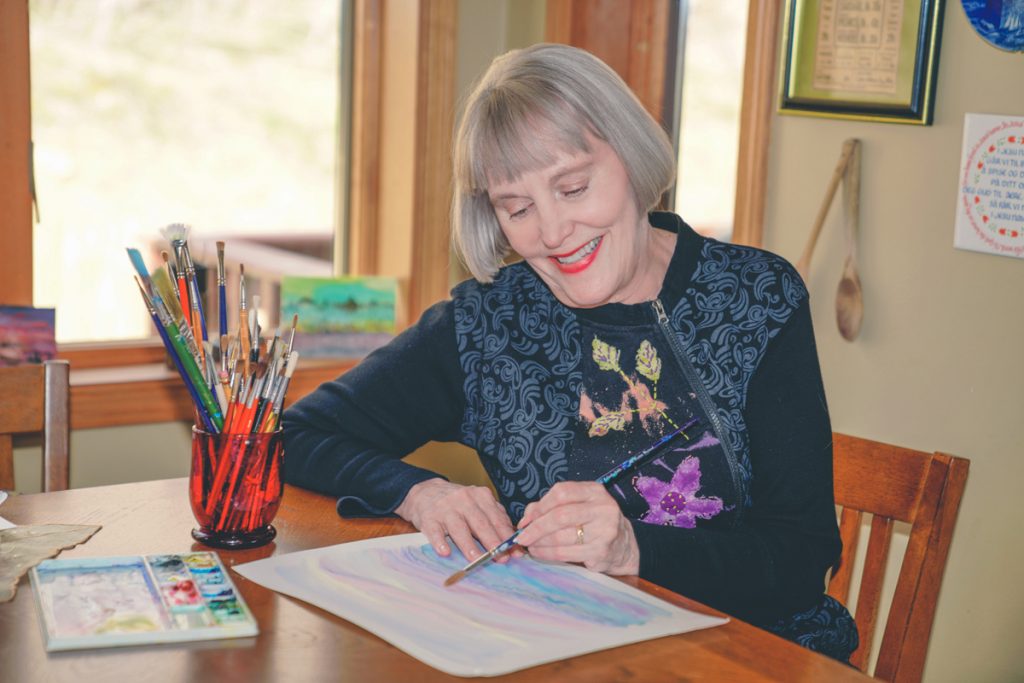 Renee is painting on a piece of paper. she is using a small brush. She is smiling.